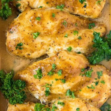 chicken breast baked with mustard sauce and parsley in a dish. social media image