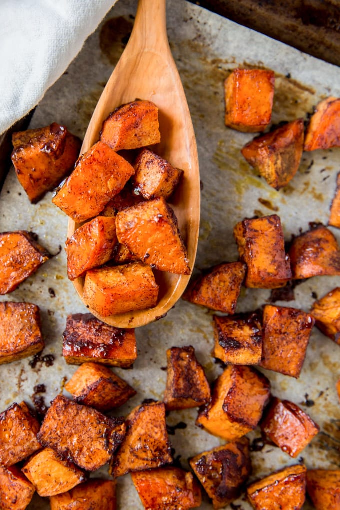 Roasted sweet potatoes on a sheet pan with a wooden spoon