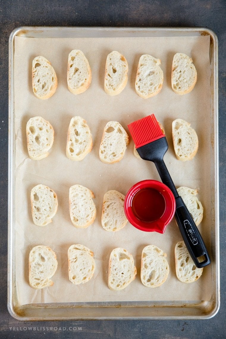 A sheet pan with slices of bread and a pastry brush and bowl of olive oil