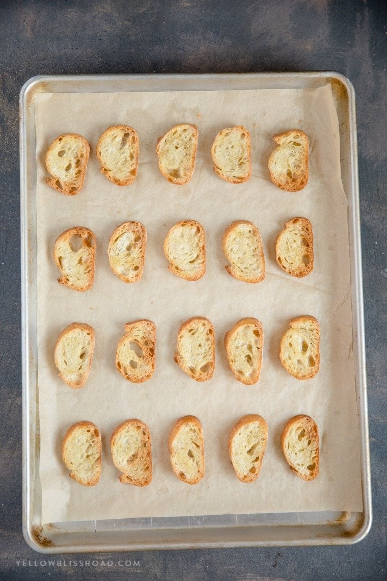 Crostini slices laid out on a parchment paper covered baking sheet.