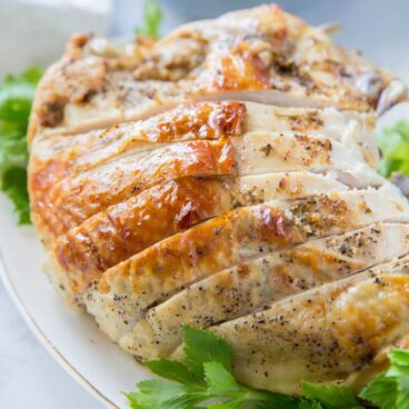 Turkey breast, browned skin, sliced and sitting on top of large pieces of parsley. Image for social media.