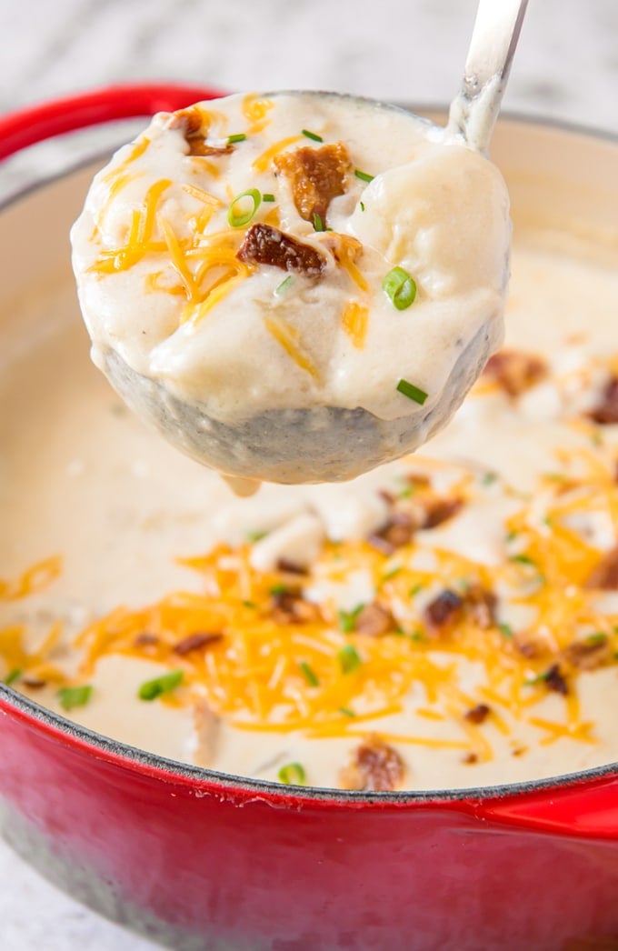 A ladle full of baked potato soup with bacon, cheese and chives on top