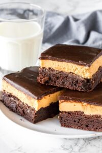 A plate of layered peanut butter brownies with a layer of peanut butter filling and chocolate on top.