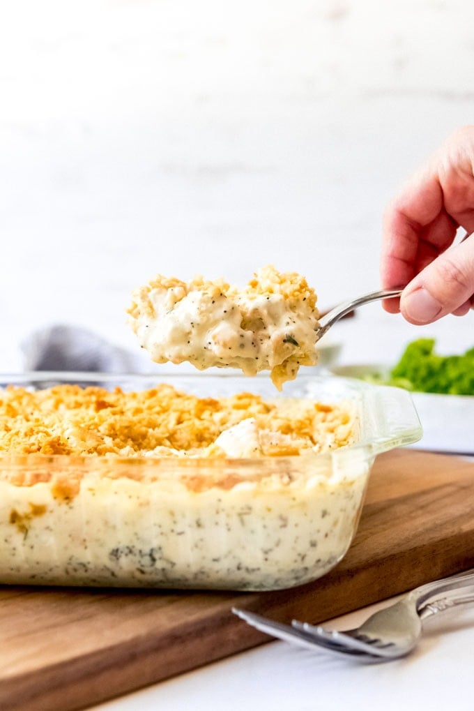 An image of a hand holding a scoop of poppy seed chicken over a baking dish.