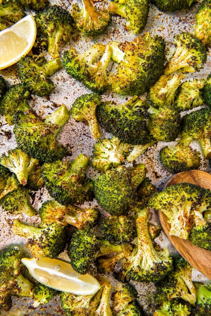 An overhead shot of roasted broccoli and lemon wedges on a sheet pan.