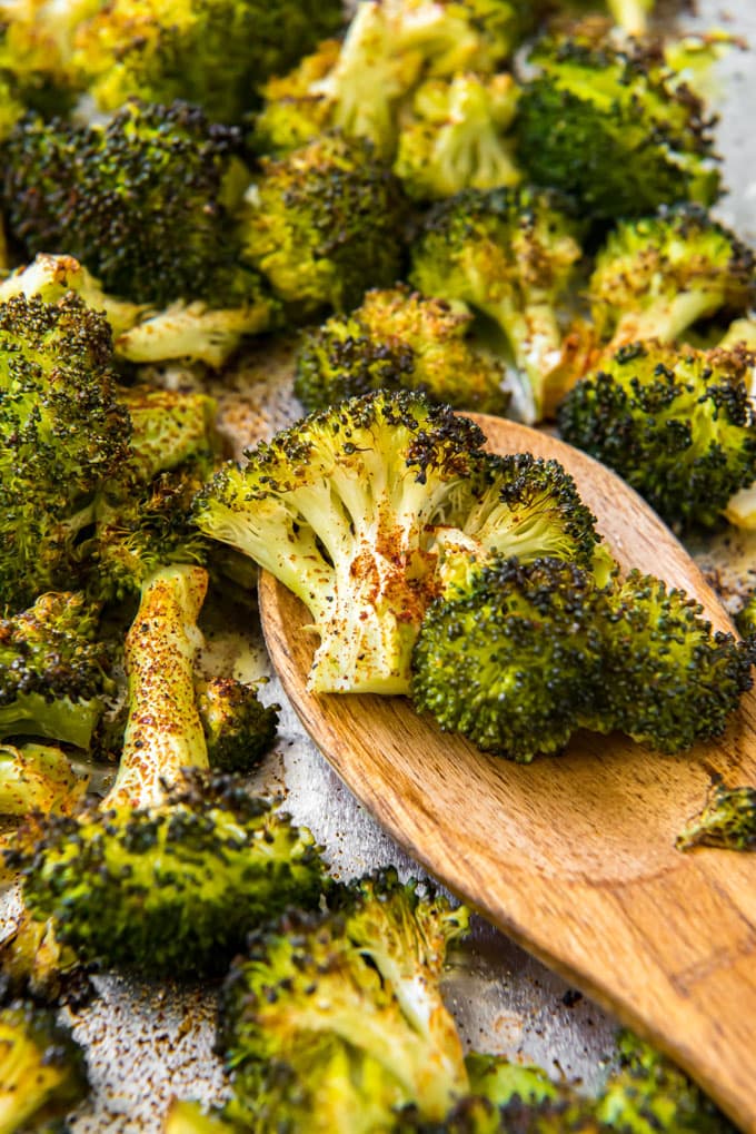 A wooden spoon holding a couple of pieces of roasted broccoli on a sheet pan