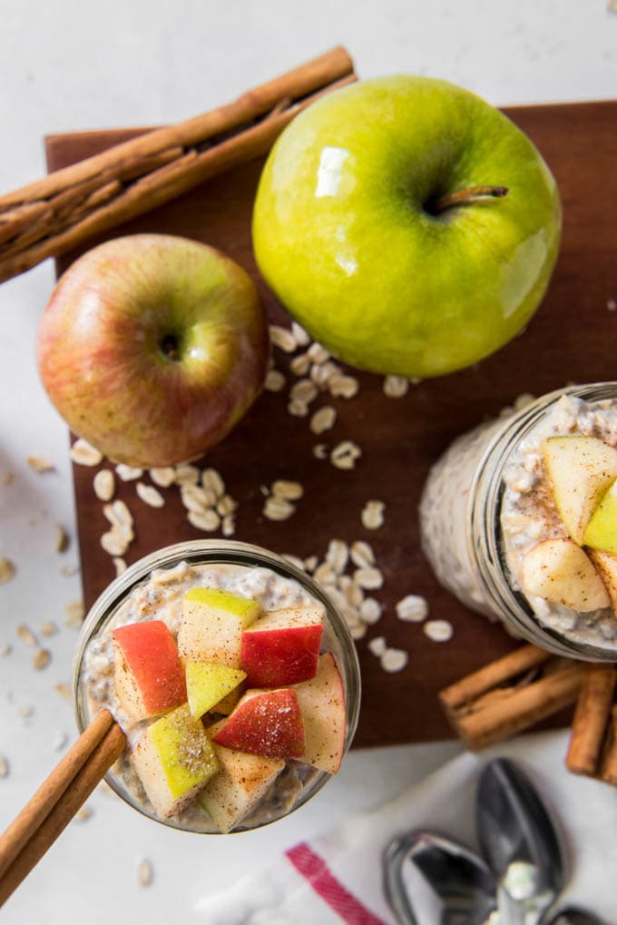 Two jars of Apple Cinnamon Overnight Oats with apples sitting on a table