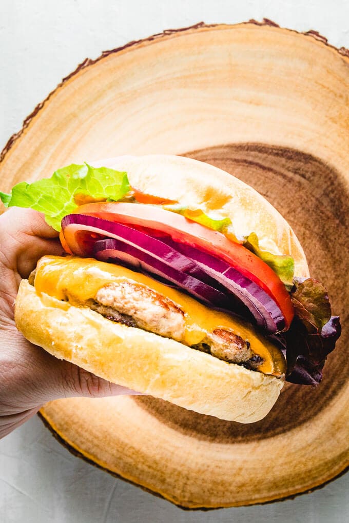 Turkey burger with lettuce, tomato, and cheese held in hand over cutting board.