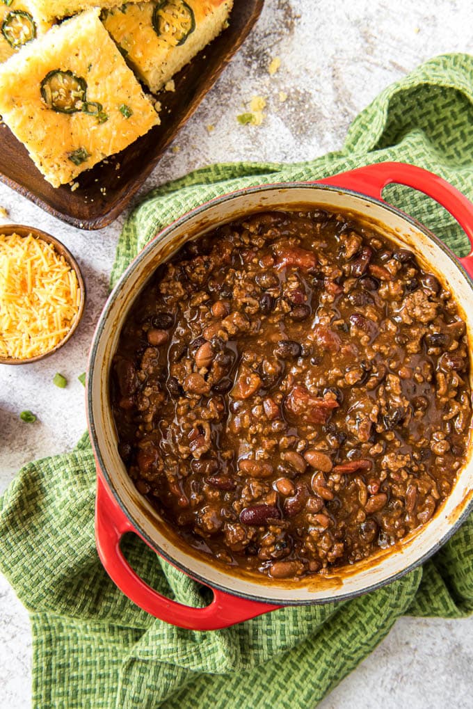 A pot of the best over chili sitting on a green towel next to a plate of cornbread