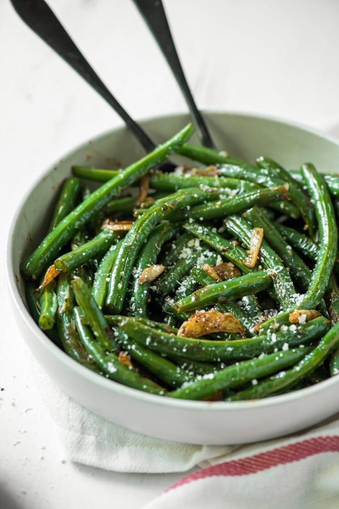 green beans with garlic in a white bowl with two serving spoons