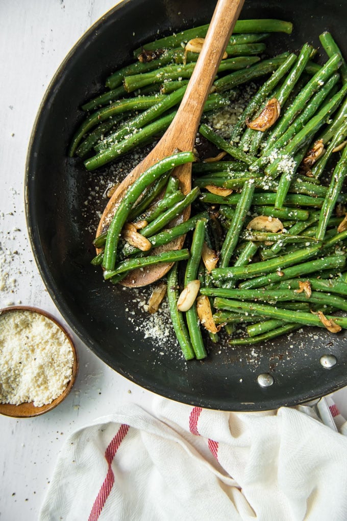 sauteed green beans with garlic and parmesan in a skillet with a wooden spoon