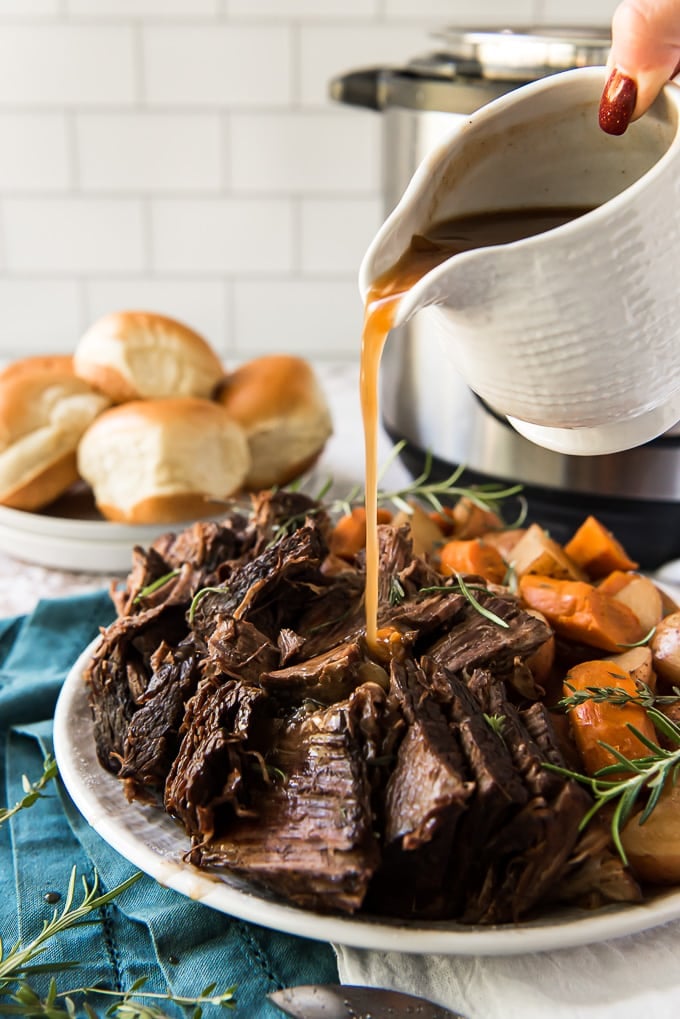 Gravy being poured over a pot roast, with an instant pot in the background.