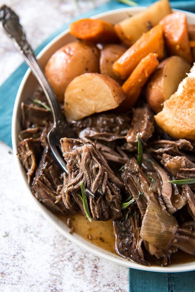A close up of a plate with pot roast and gravy, potatoes and carrots.