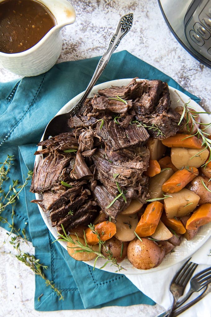 An overhead image of instant pot pot roast on a plate with carrots, potatoes and gravy.