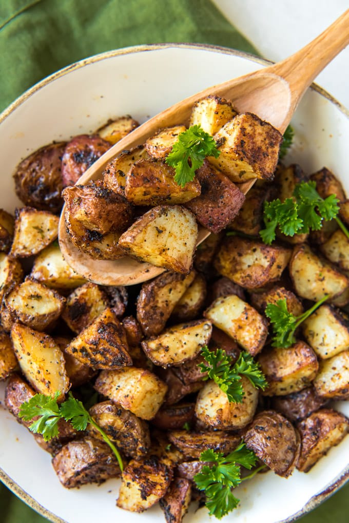 diced red potatoes in a white dish with a wooden spoon and parsley