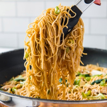 Chow Mein noodles with tongs in a frying pan.