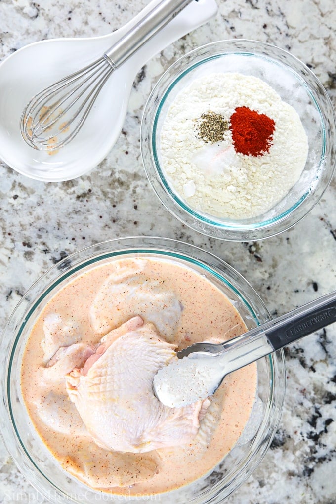 These simple and delicious fried chicken thighs are so irresistibly crunchy and flavorful. This easy recipe will become a staple in your home. #friedchicken #chickenthighs #crispychicken #easychicken an overhead photo of chicken thighs being dipped into buttermilk with the flour breading mixture in a bowl beside it