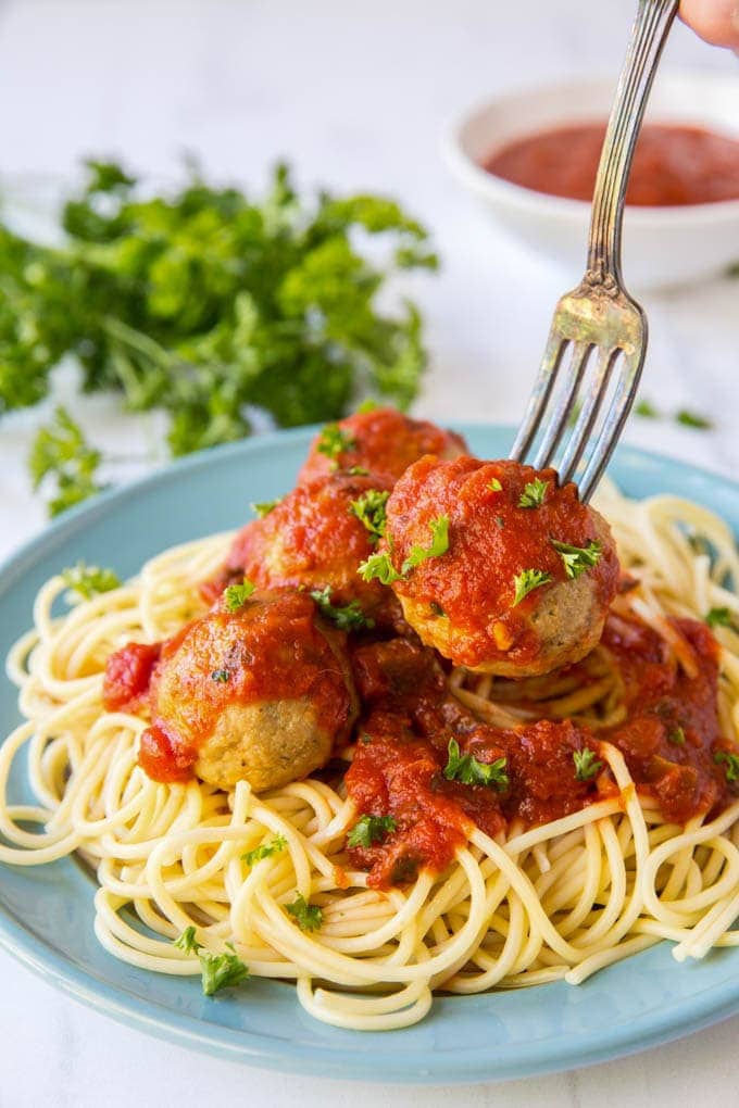 a fork stuck into a meatball, lifting it up off of a plate of spaghetti.