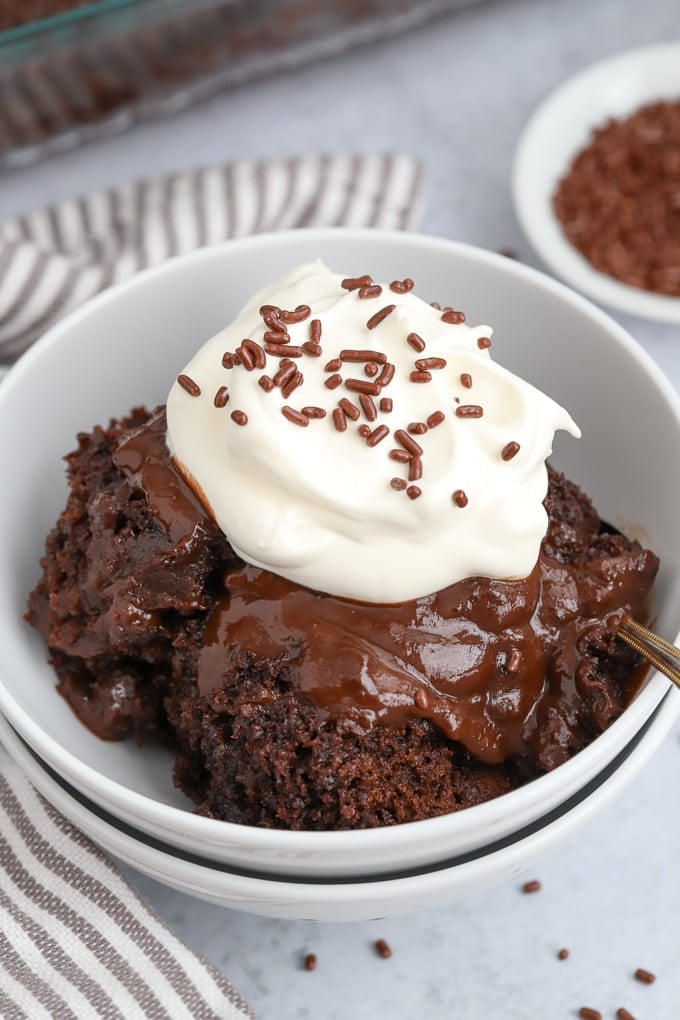 Chocolate Pudding Cake in a white bowl topped with whipped cream and chocolate sprinkles.