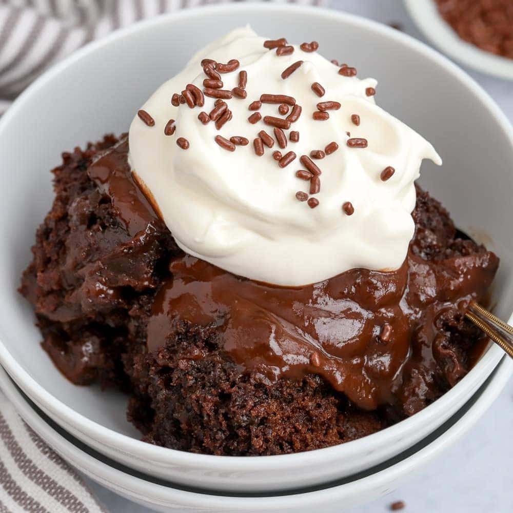 Chocolate Pudding Cake in a white bowl topped with whipped cream and chocolate sprinkles.