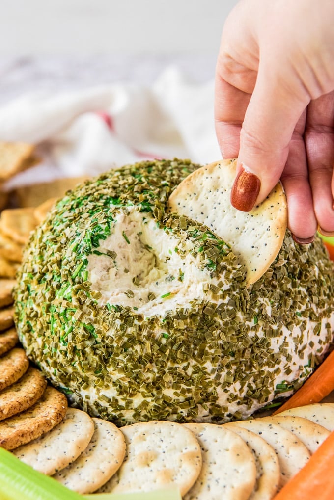 a hand reaching in and scooping a bite of crab dip cheese ball on a cracker.