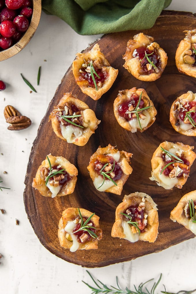 an overhead image of cranberry brie bites on a wooden platter with fresh rosemary