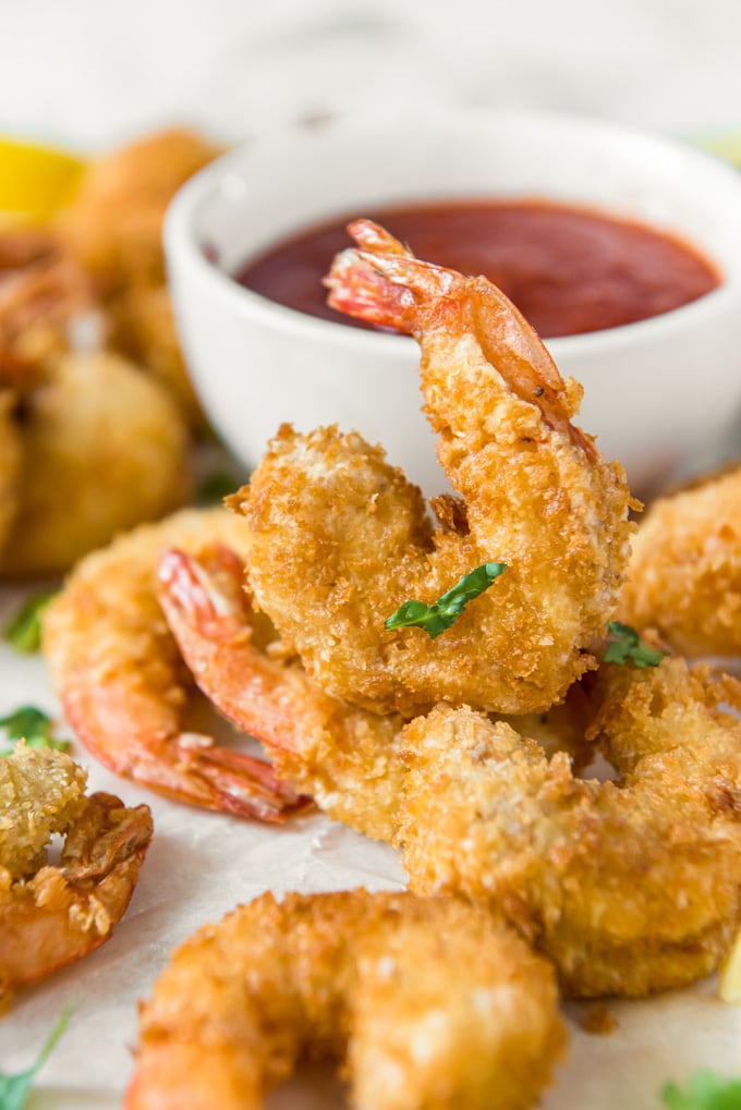 a platter of fried shrimp next to a dish of cocktail sauce with one shrimp sitting with it's tail up