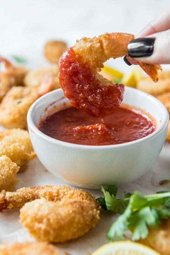 A hand dipping a fried shrimp into cocktail sauce.