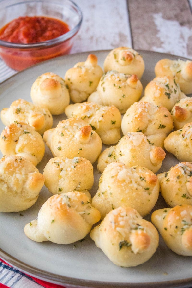 Mini Parmesan Garlic Knots are a poppable appetizer that flies off the plate! Serve them small, or make bigger knots to serve up with your favorite dinners! garlic knots on a plate