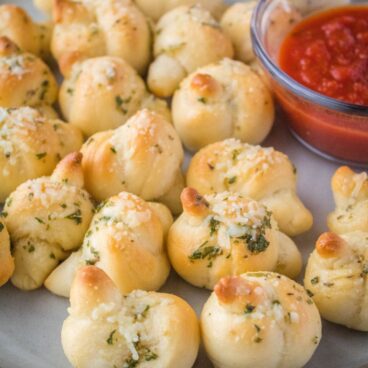 Mini Parmesan Garlic Knots are a poppable appetizer that flies off the plate! Serve them small, or make bigger knots to serve up with your favorite dinners!
