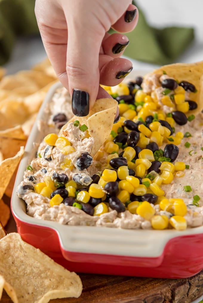 hand holding a chip dipping into dip with corn and black beans