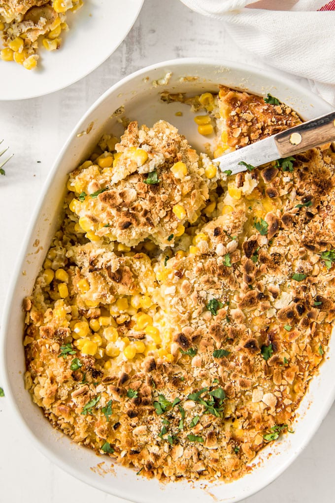 A casserole dish filled with scalloped corn casserole with a metal spoon