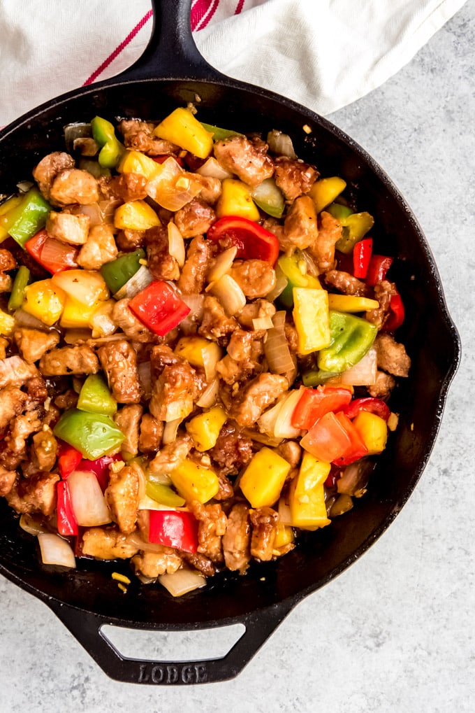 An image of sweet & sour pork in a cast iron skillet with red and green bell peppers, onions, and pineapple.