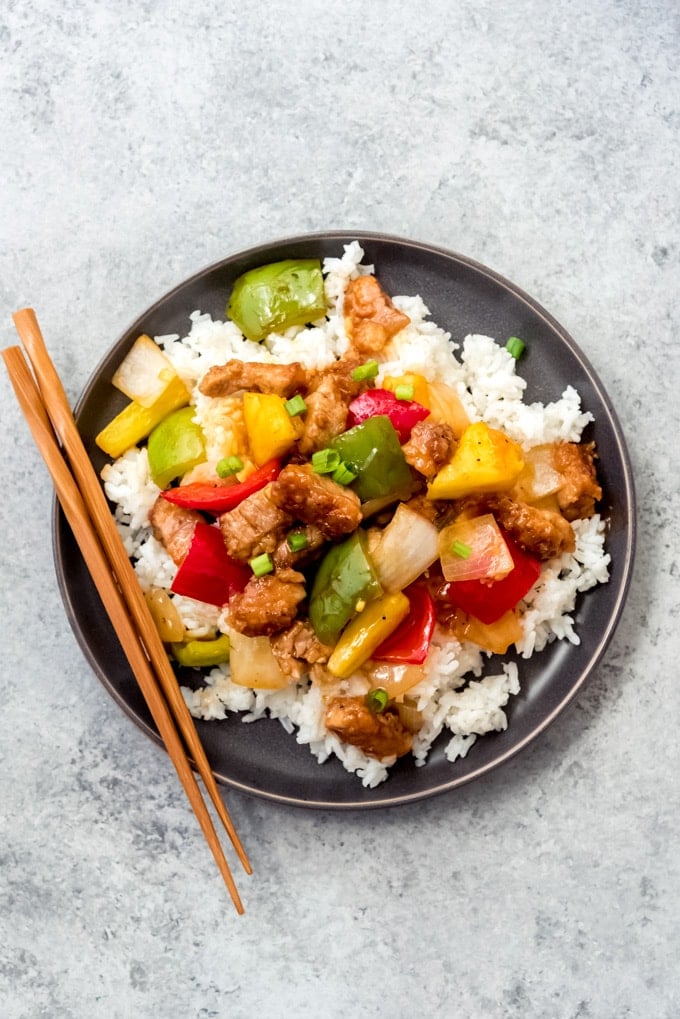 Rice on a plate topped with sweet and sour pork and veggies.