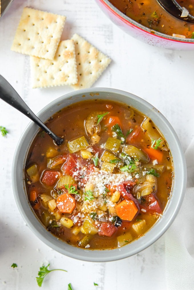 a bowl of vegetable soup with a spoon and crackers