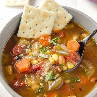 A bowl of vegetable soup with saltine crackers
