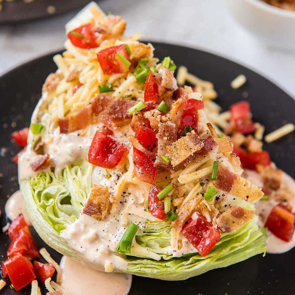 A plate of wedge salad with dressing, bacon, cheese, and tomatoes on top