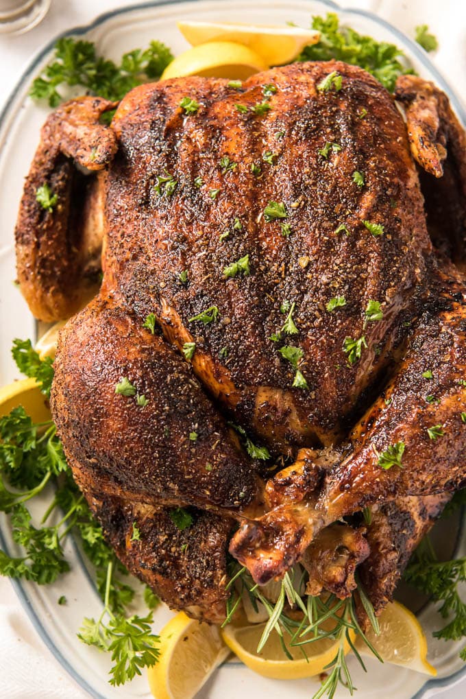 An overhead view of a whole roast chicken on a platter surrounded by lemon slices