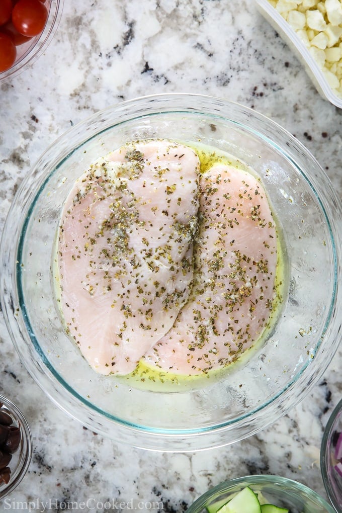 an overhead image of chicken marinating in a bowl for greek chicken salad