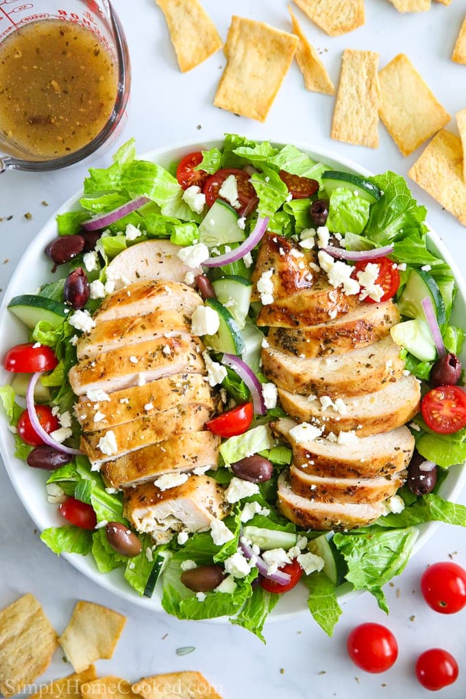 The BEST Greek Chicken Salad with with juicy grilled chicken, crunchy cucumbers, cherry tomatoes, and crumbled feta cheese. #greekchickensalad #greeksalad #chickensalald #greeksaladdressing #grilledchicken An overhead image of Greek chicken salad with sliced chicken breast, cucumbers, tomatoes, and feta cheese on top.