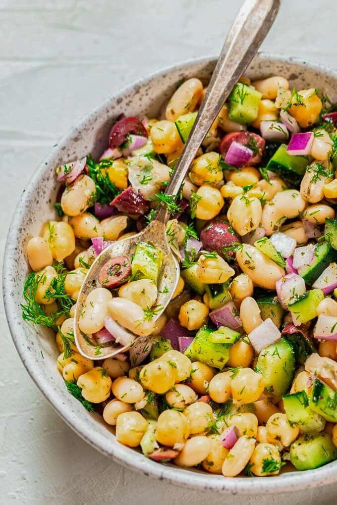 A salad of beans, cucumber, onions olives and dill with a spoon.