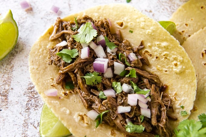 Instant Pot Barbacoa Beef tacos topped with onion, cilantro, and a squeeze of lime