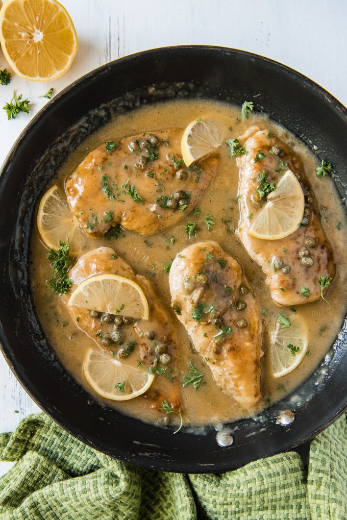 four pieces of chicken piccata and lemon piccata sauce in a large skillet with capers and lemon slices