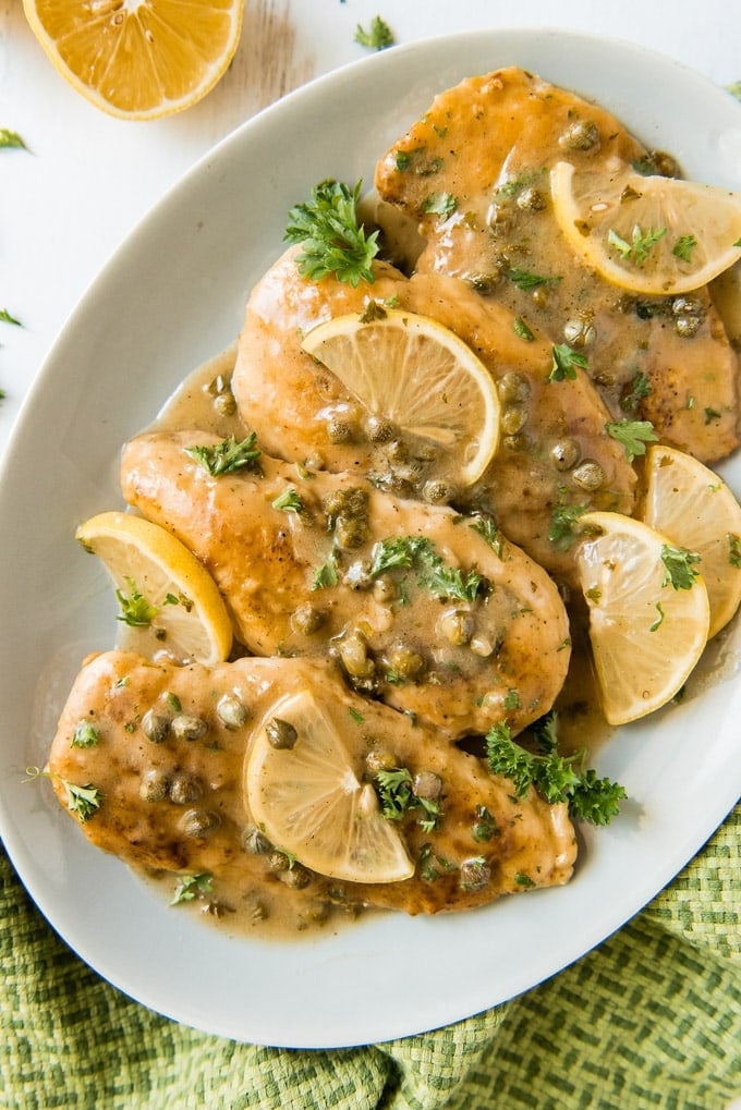 An overhead photo of four pieces of chicken piccata with picatta sauce, capers and lemon slices.