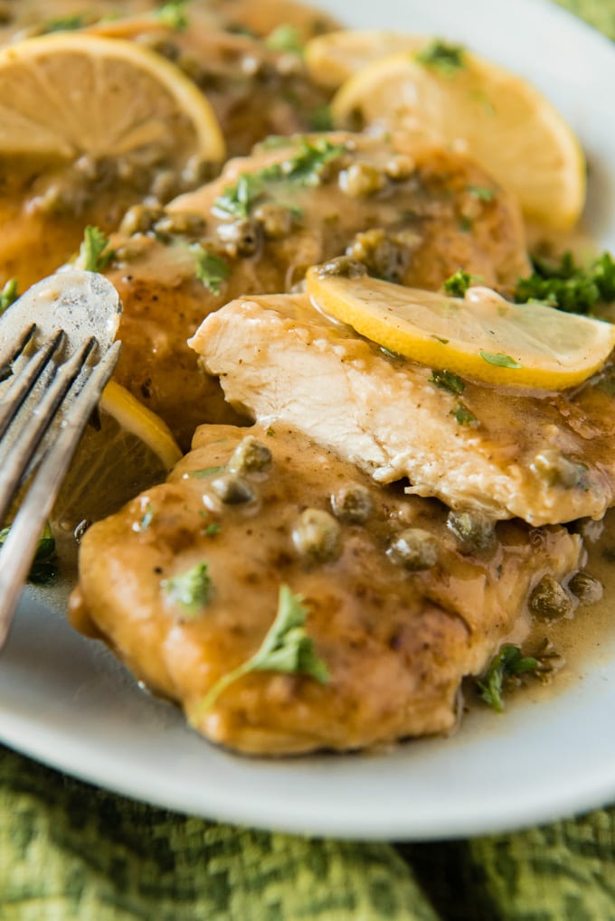 A close up image of a piece of chicken with lemon sauce and capers cut in half