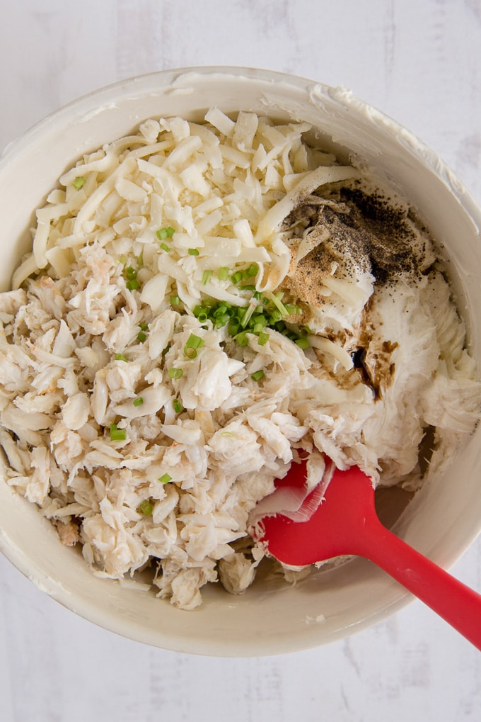 crab, chives, cheese and seasoning in a mixing bowl with a red spatula.