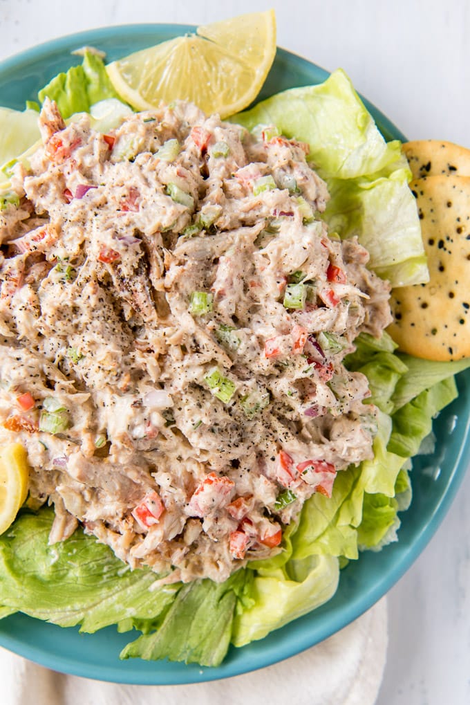 A large portion of homemade crab salad with fresh lump crabmeat on a bed of lettuce with lemon wedges and crackers.