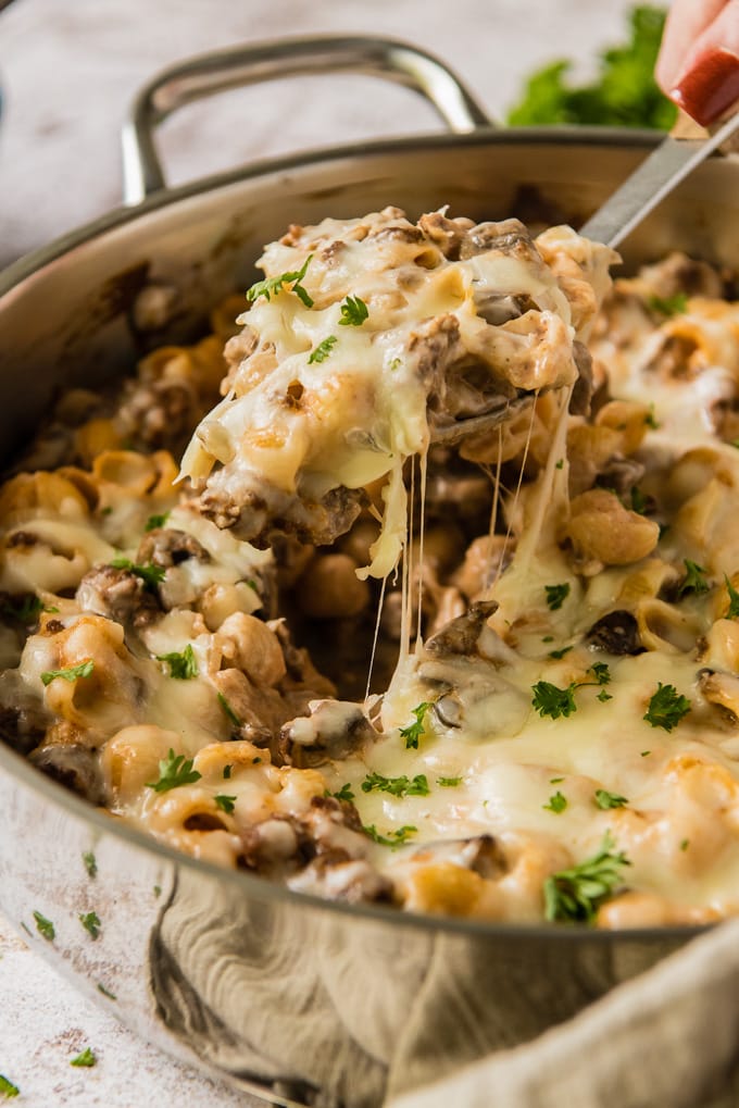 A scoop of hamburger pasta casserole out of a large skillet