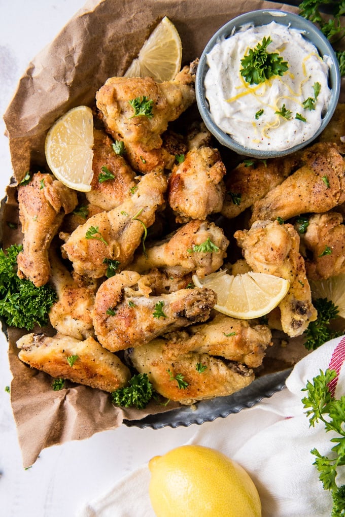 an overhead shot of crispy chicken wings with lemon slices and yogurt dip