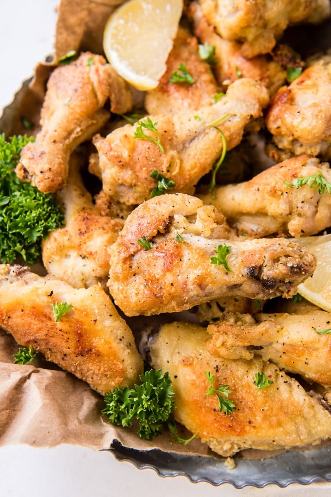 A platter full of baked chicken wings close up with lemon slices